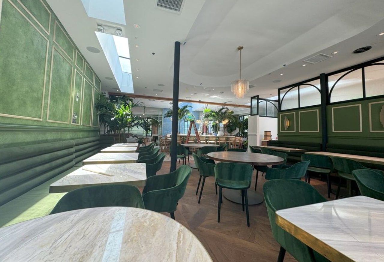 Chandelier, wall sconces and recessed lights above green banquette seating and dining tables, with installation materials still present.