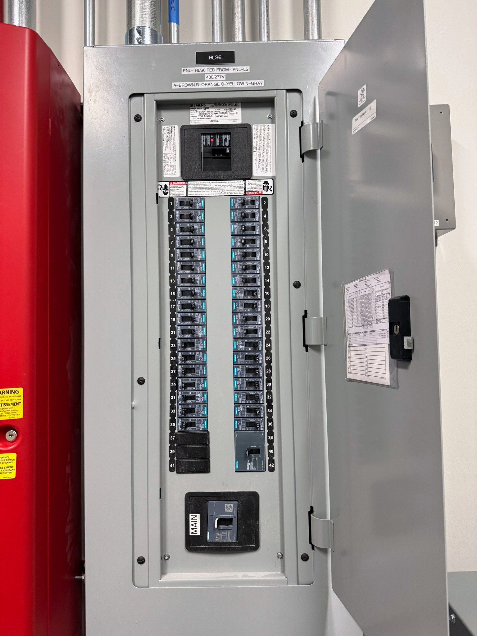 Open electrical panel with two columns of labeled breakers, main disconnects and overhead metal conduit at the Violet project.