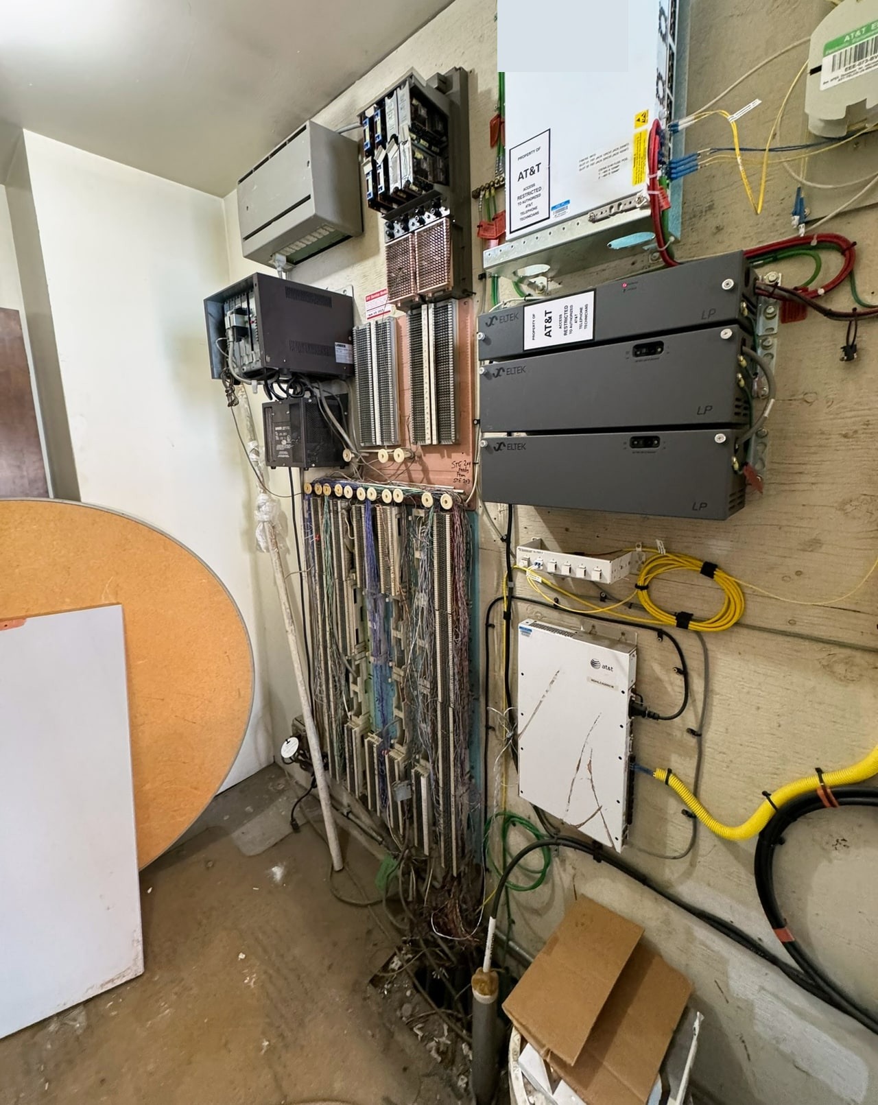 Wall-mounted telecommunications equipment with terminal blocks, cable connections and coiled yellow fiber cable.