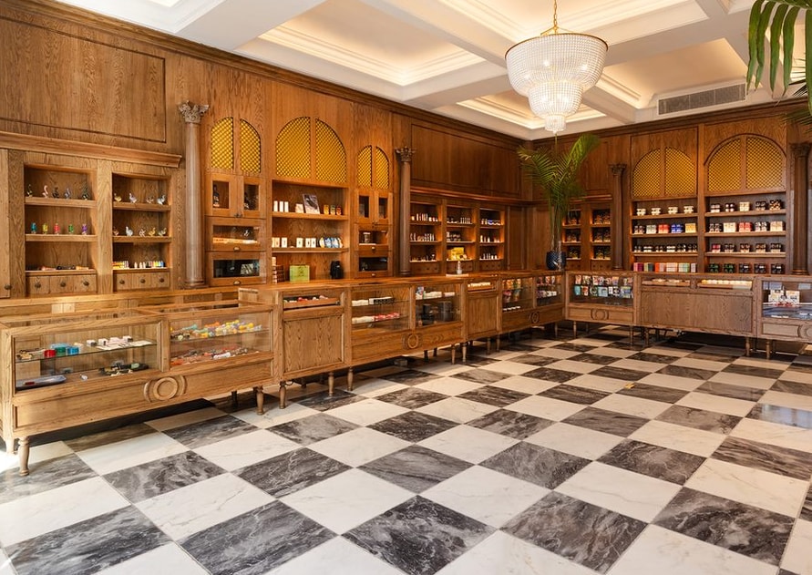 Chandelier, illuminated ceiling coves and warm display-shelf lighting above wooden retail counters and a black-and-white tiled floor.