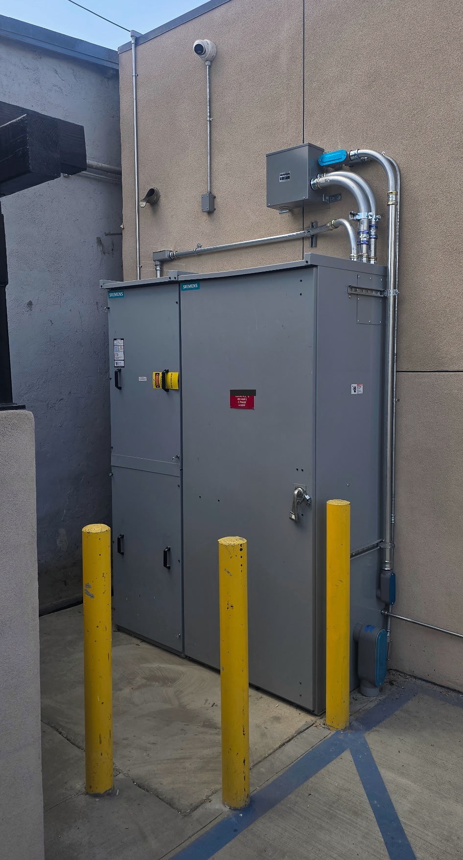 600A single-meter electrical service cabinet at a veterinary hospital in Lynwood, with conduit and three yellow protective bollards.